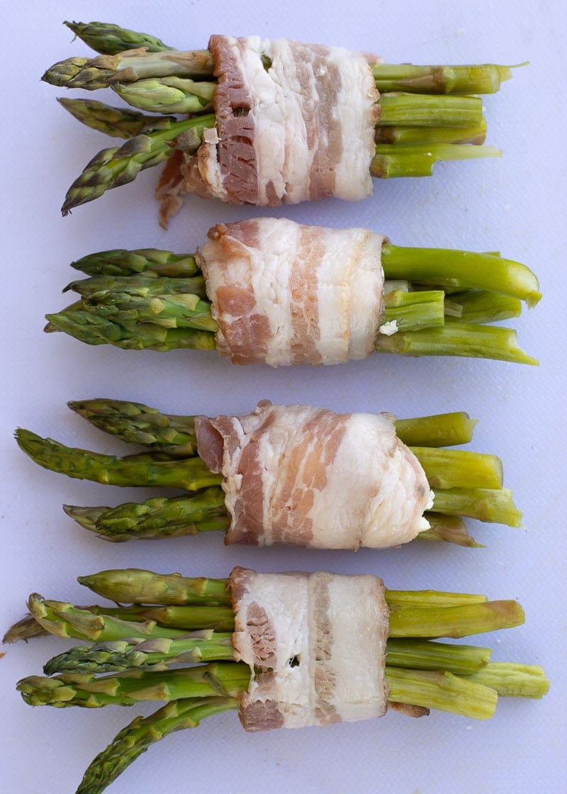 Four bundles of uncooked asparagus with cheese wrapped in uncooked bacon