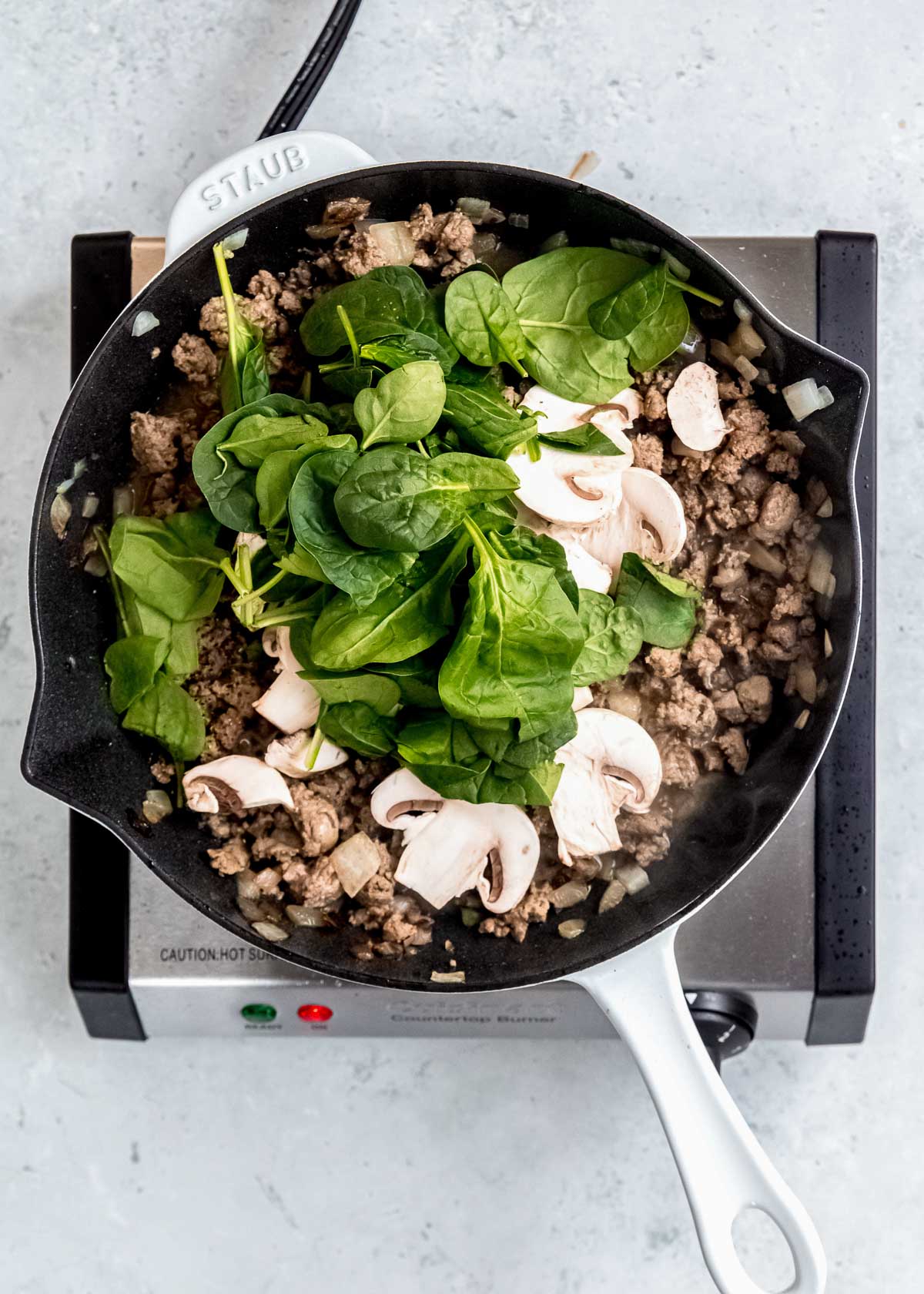 spinach and mushrooms being added to black skillet with breakfast sausage