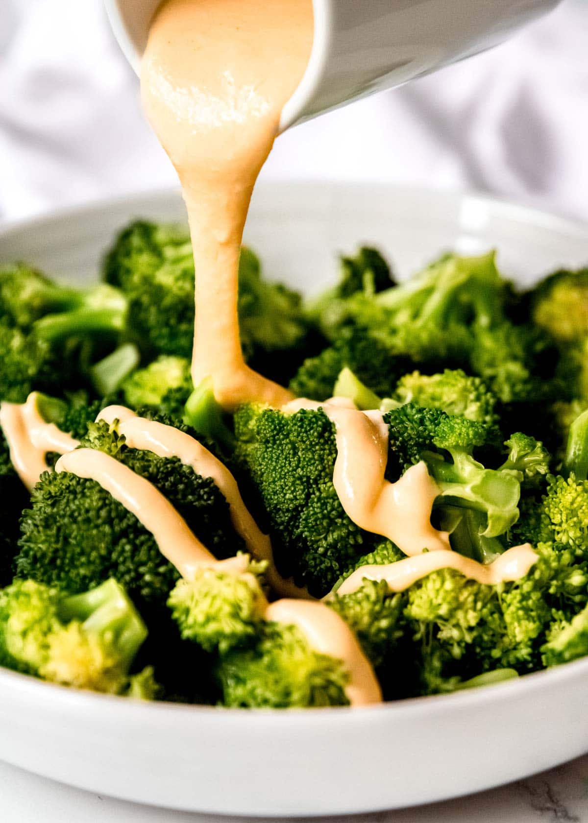 cheese sauce being poured on steamed broccoli