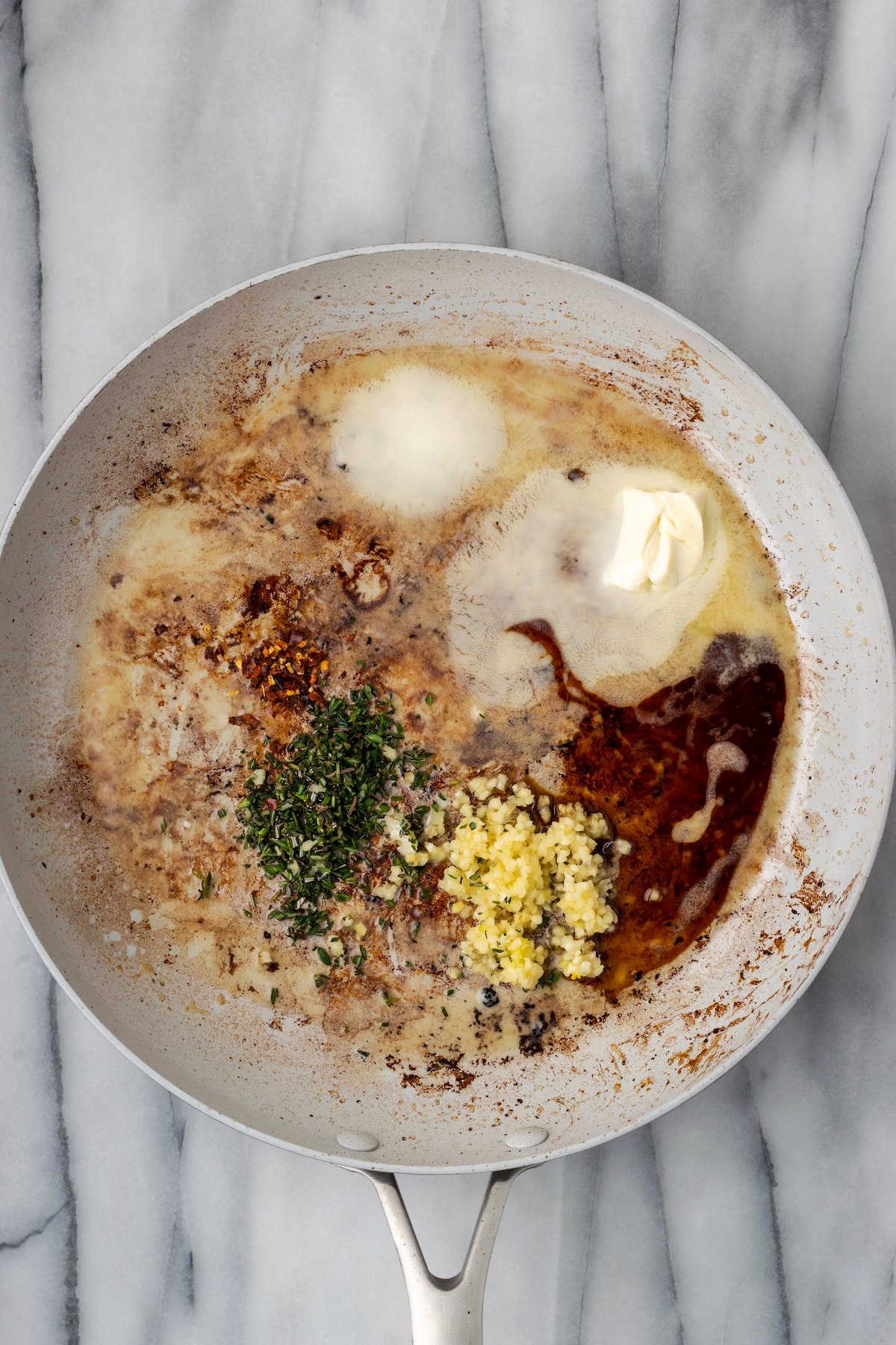 A skillet with butter, garlic, herbs, soy sauce, and chili flakes in it