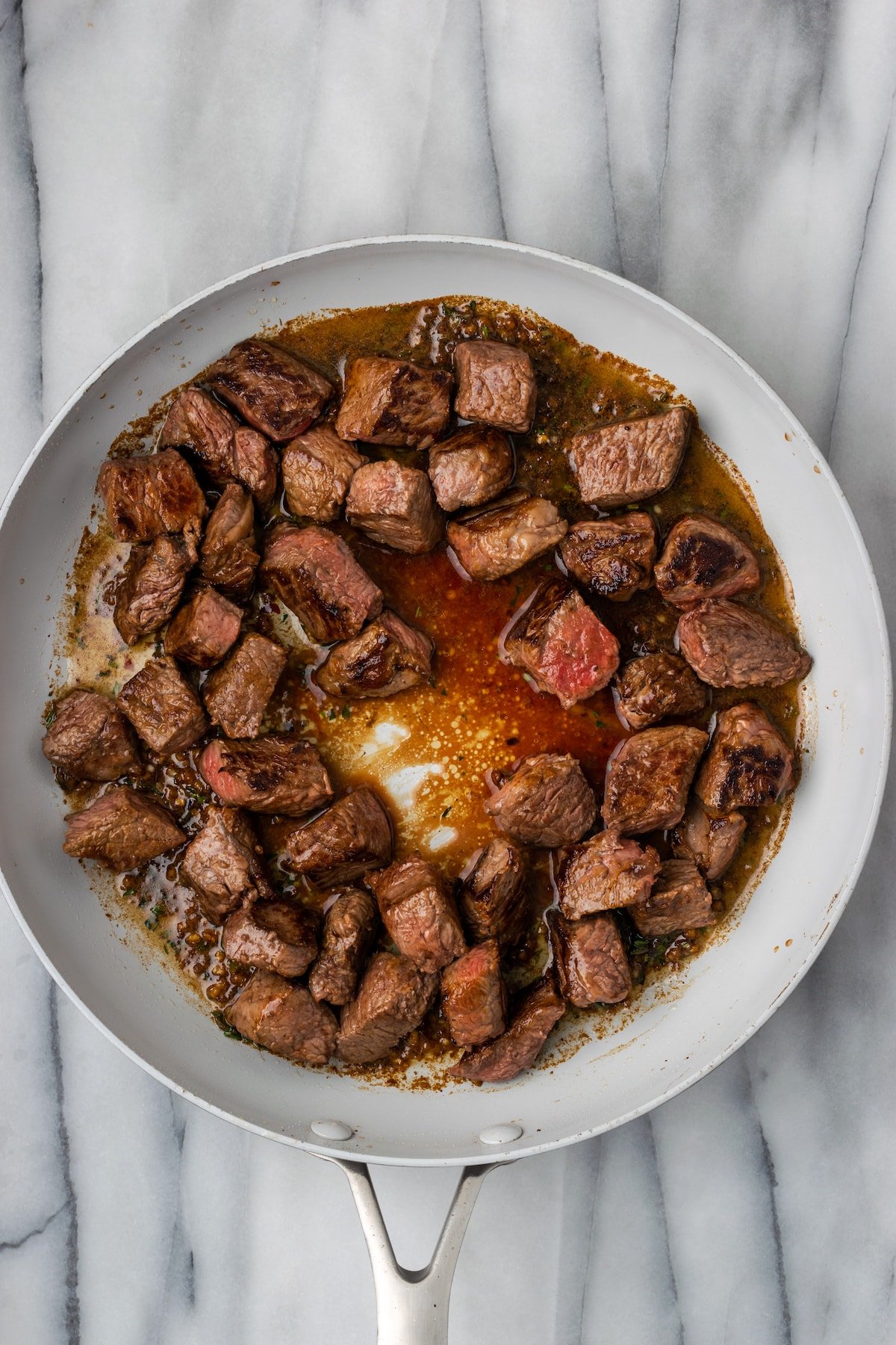 Overhead view of steak bites in a skillet cooking in a sauce