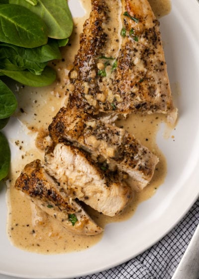 Close up overhead view of garlic parmesan chicken, with half of it cut into slices, on a plate next to some greens