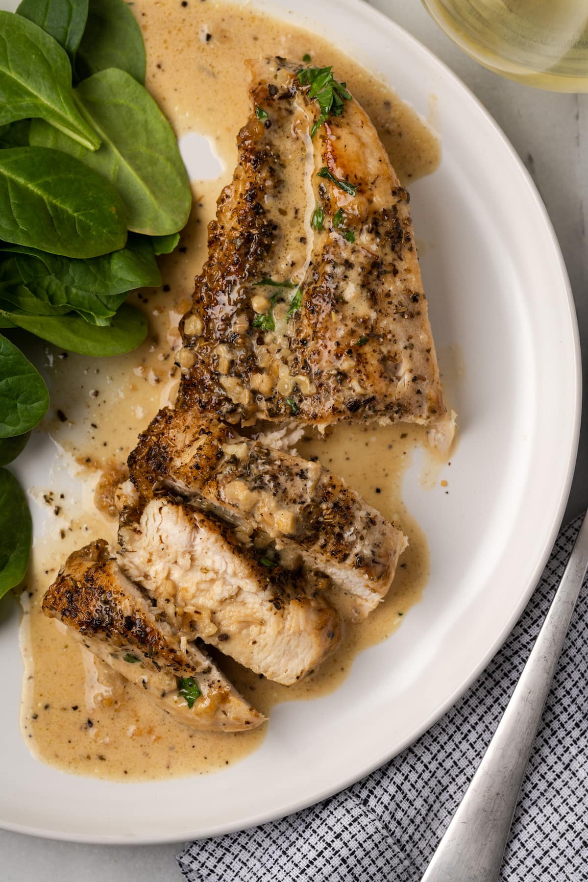 Overhead view of garlic parmesan chicken on a plate next to a salad, with half of it cut into slices