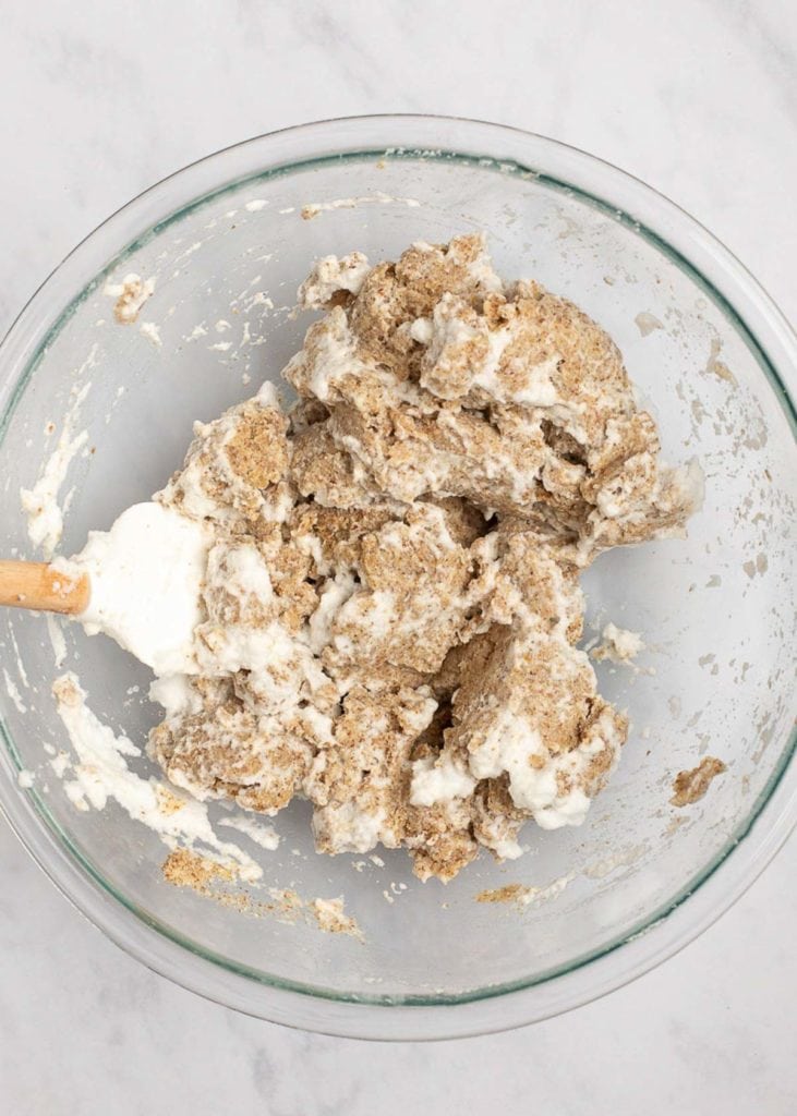 A mixing bowl with a rubber spatula folding whipped egg whites into dough