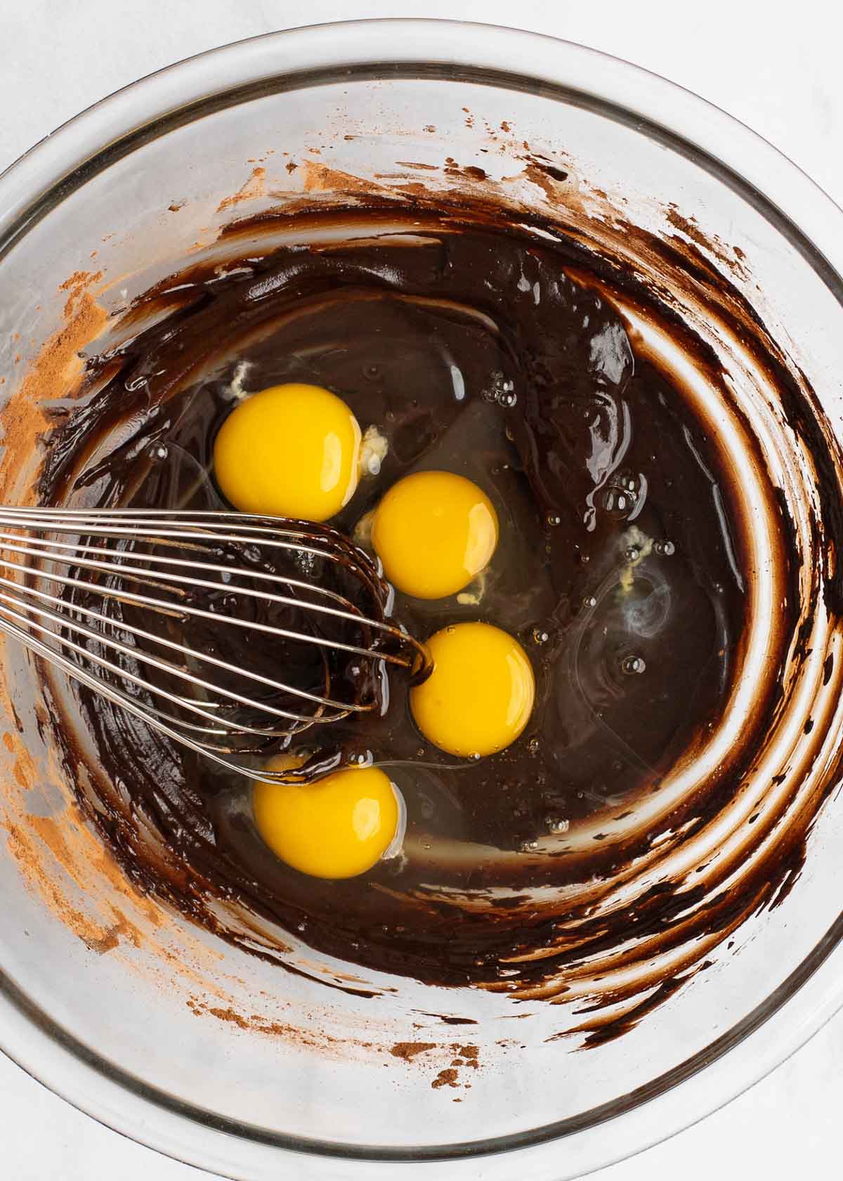 Overhead view of four eggs in a mixing bowl, on top of cocoa powder mixed with butter