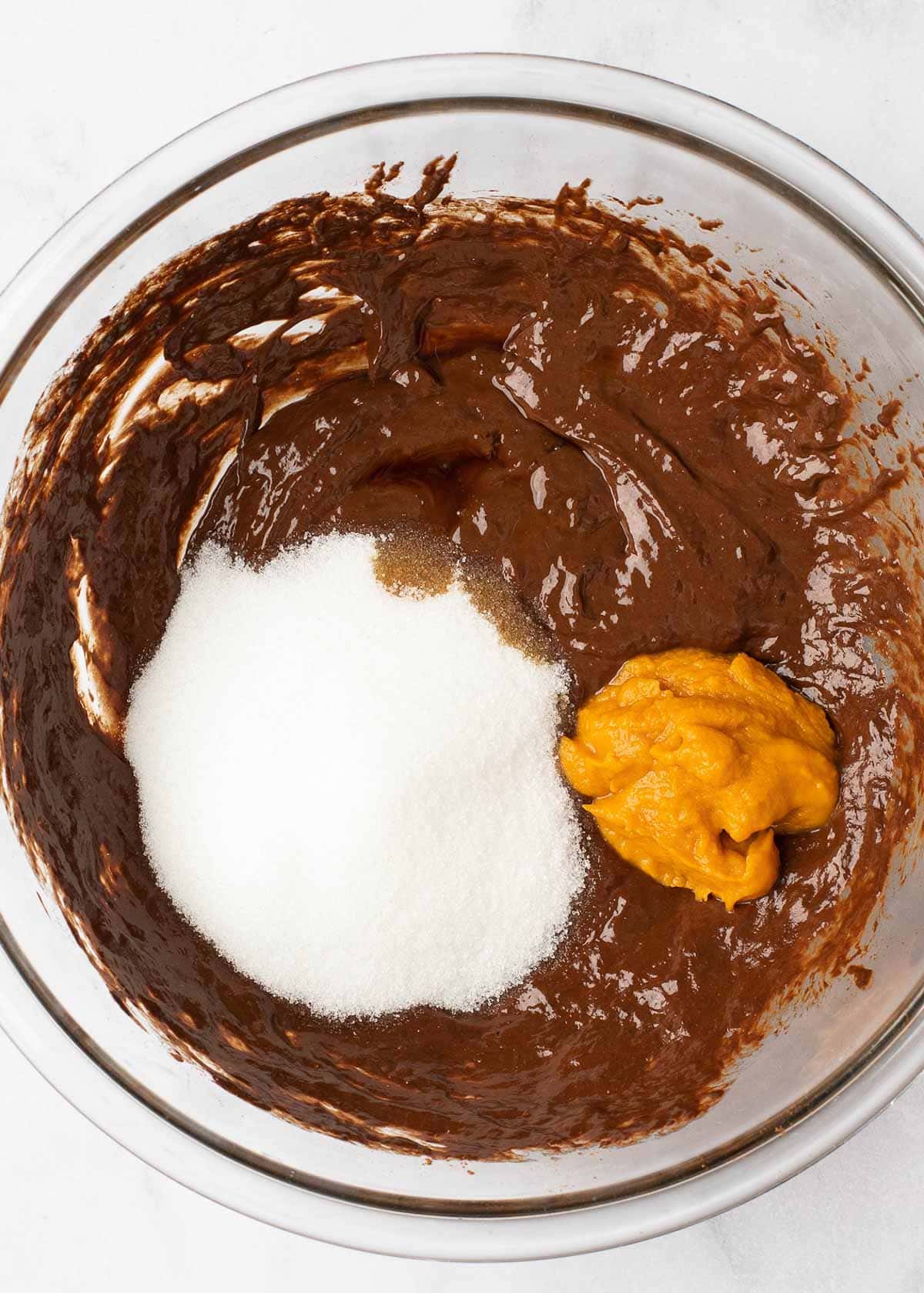 Overhead view of pumpkin puree, monkfruit sweeter, and vanilla extract on top of a chocolate batter in a mixing bowl