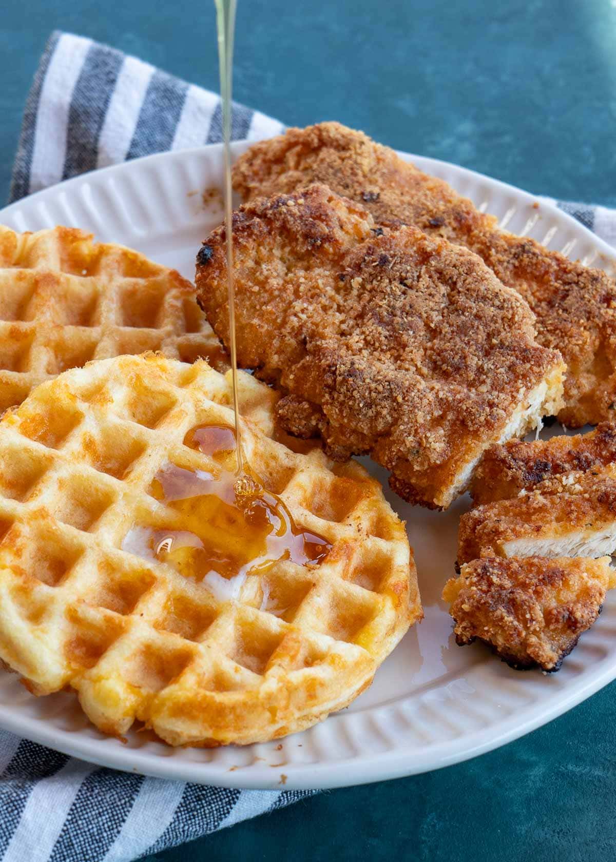 shot of sugar free maple syrup being poured on waffles with crispy chicken tenders