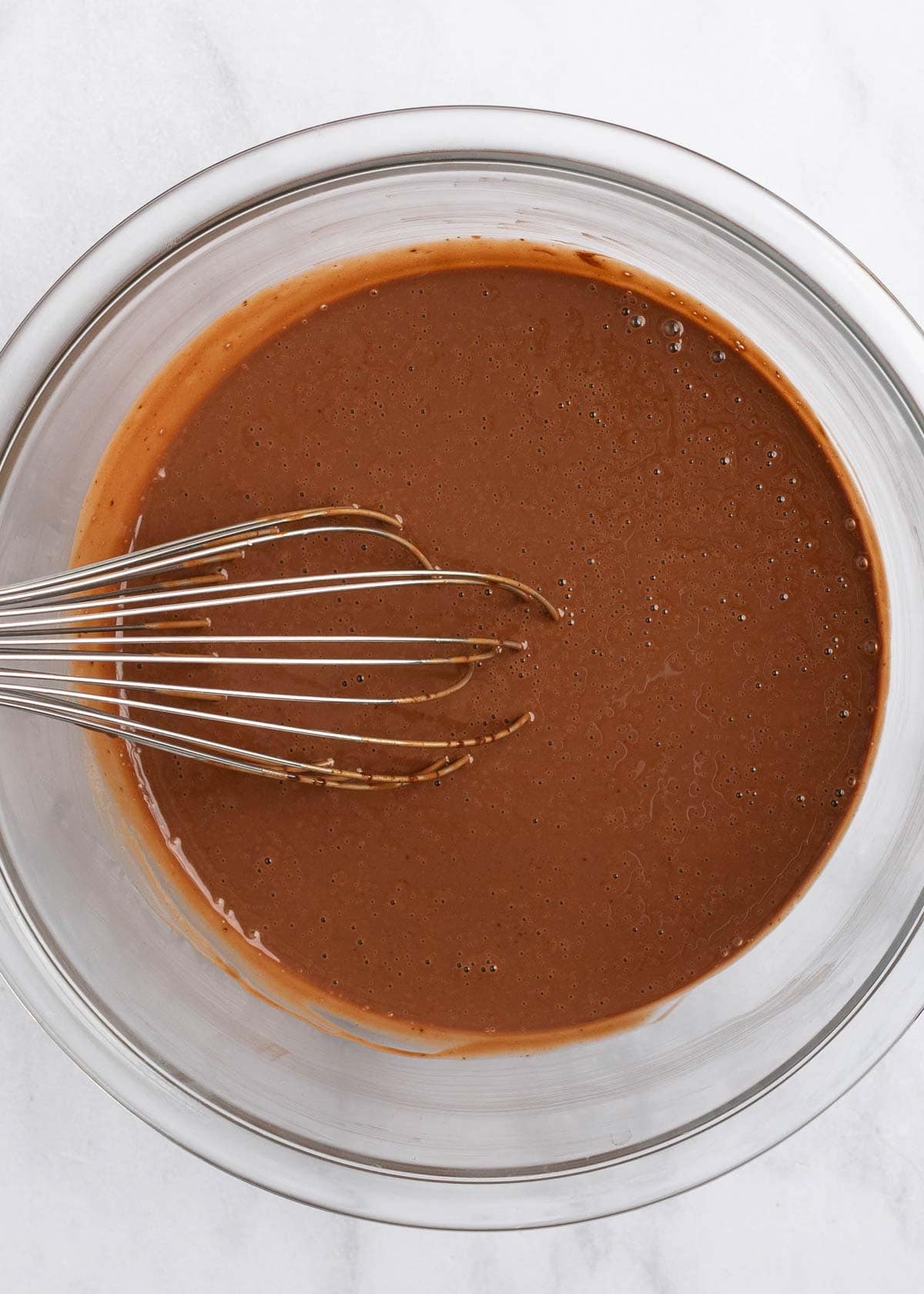 A bowl of chocolate chips and coconut cream melted together, with a whisk in it