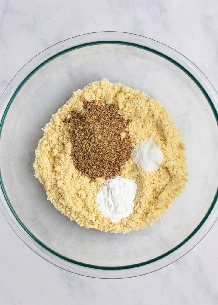 A mixing bowl full of almond flour, with a pile of flaxseed meal, a pile of baking powder, and a pile of salt