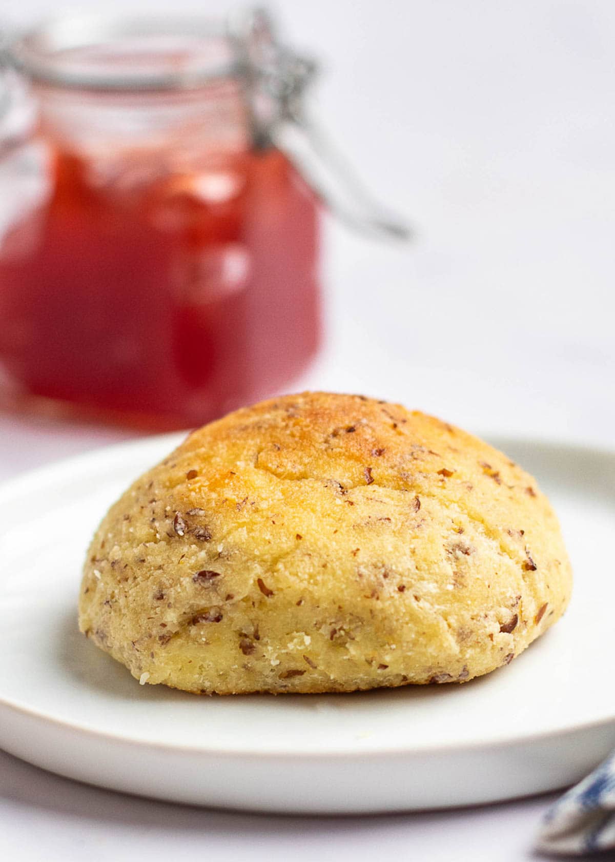 A dinner roll on a white plate, with a jar of jam in the background