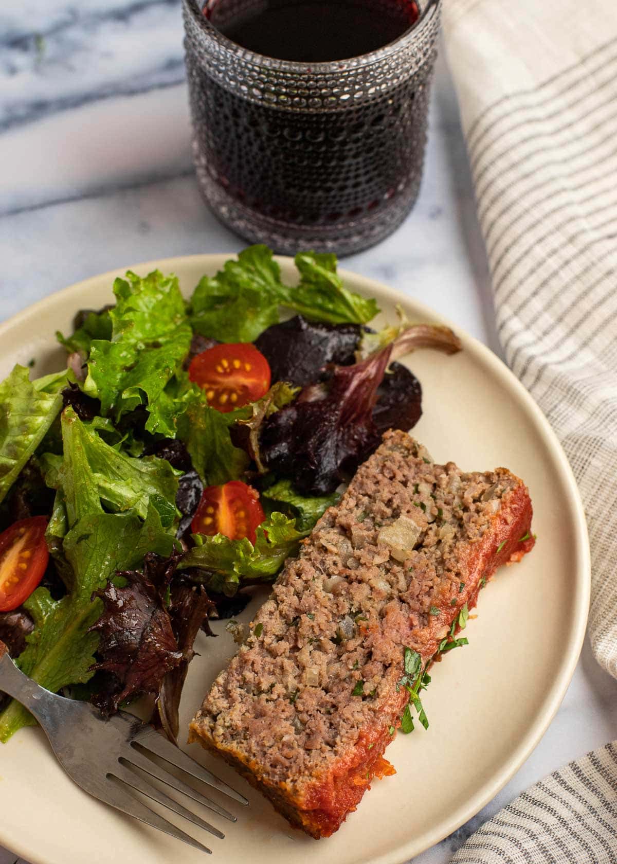 A plate with a salad and a slice of meatloaf, with a fork in front of it and a drink behind it