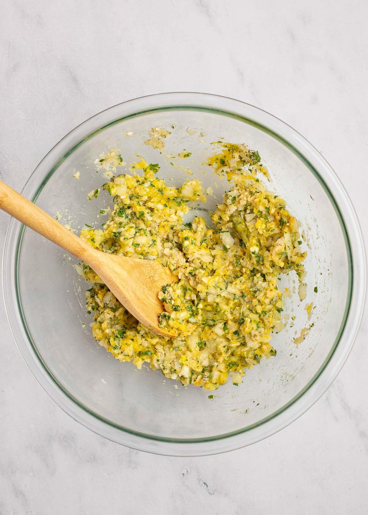 Overhead view of a seasoning mixture in a mixing bowl, with a wooden spoon