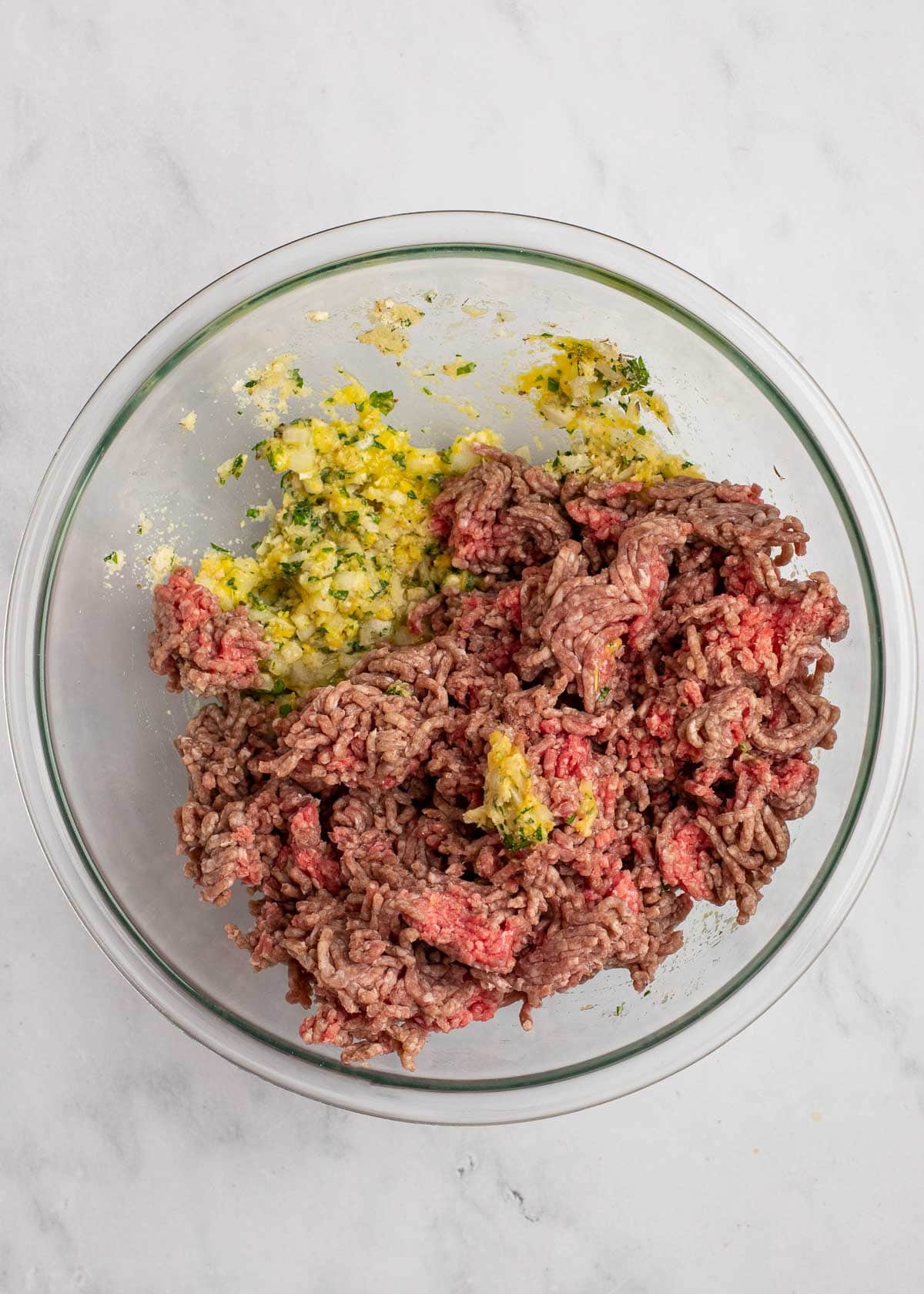 Overhead view of a mixing bowl filled with seasonings, with ground beef on top