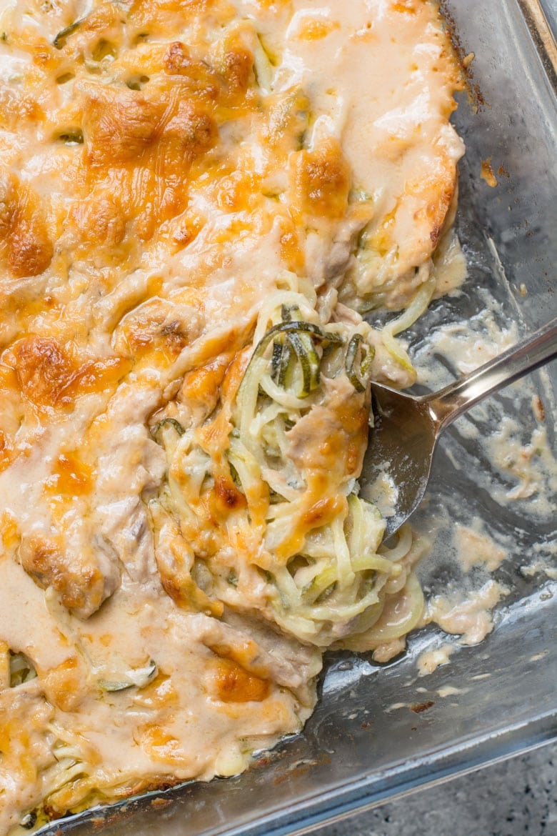 Overhead view of healthy tuna noodle casserole being scooped from a glass baking dish. 