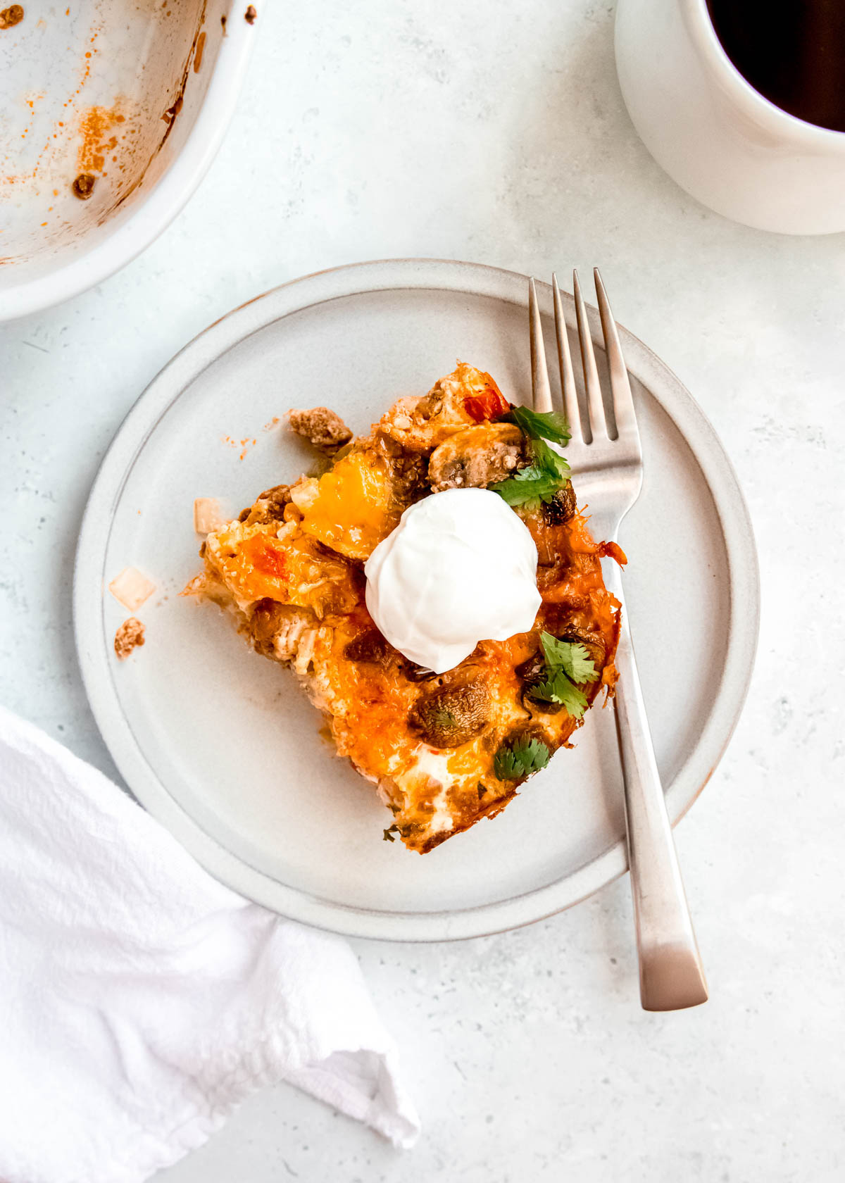 overhead shot of single slice of low carb breakfast casserole garnished with sour cream on a white plate with a fork