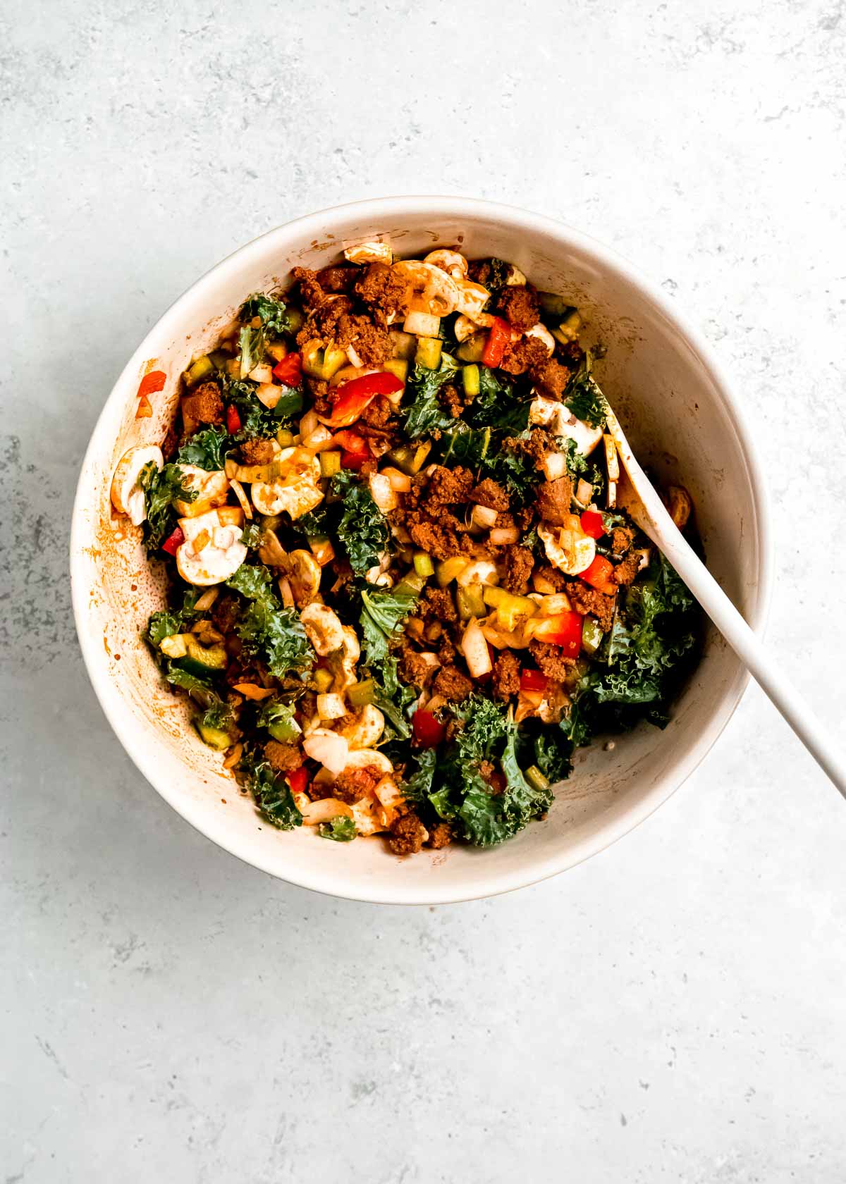 vegetables and sausage mixed up in a white bowl with a white spoon