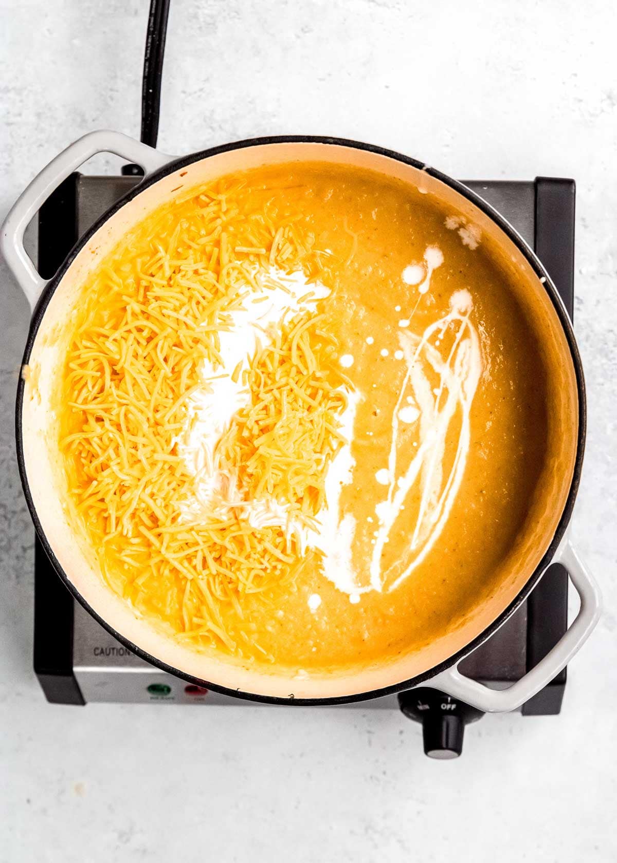 cheese and heavy cream being added to cauliflower soup in dutch oven