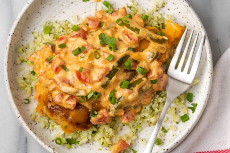 A plate of Santa Fe Chicken on top of cauliflower rice, topped with scallions, with a fork