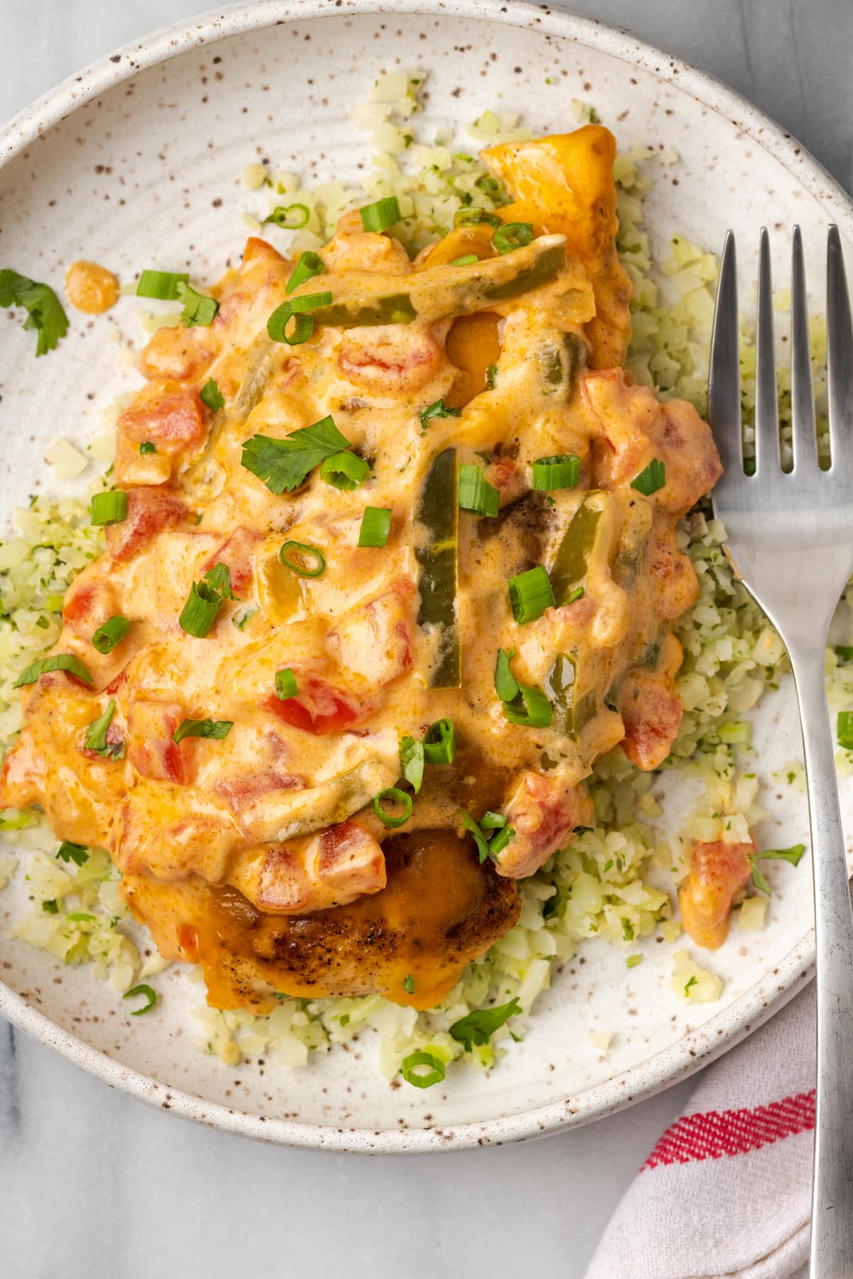 A plate of Santa Fe Chicken on top of cauliflower rice, topped with scallions, with a fork