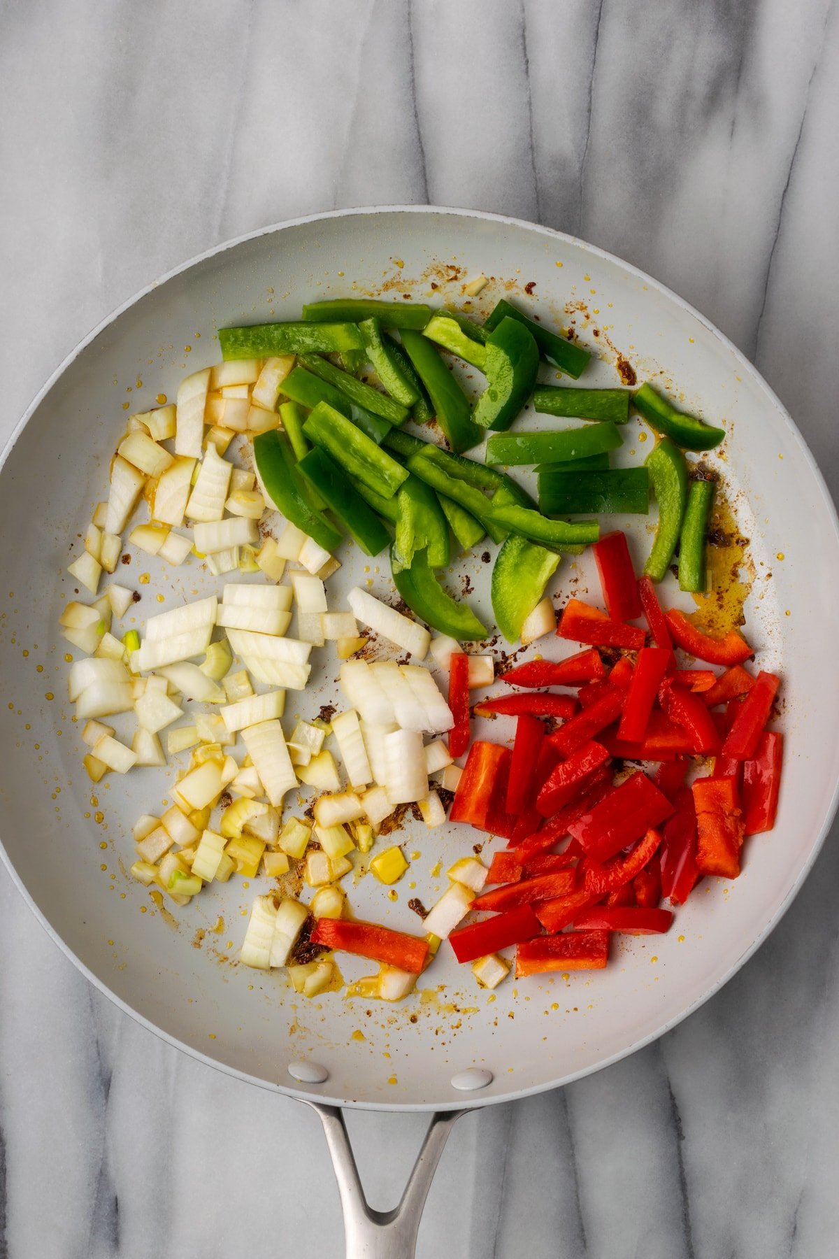 Overhead view of raw red and green bell peppers, onions, and garlic in a skillet