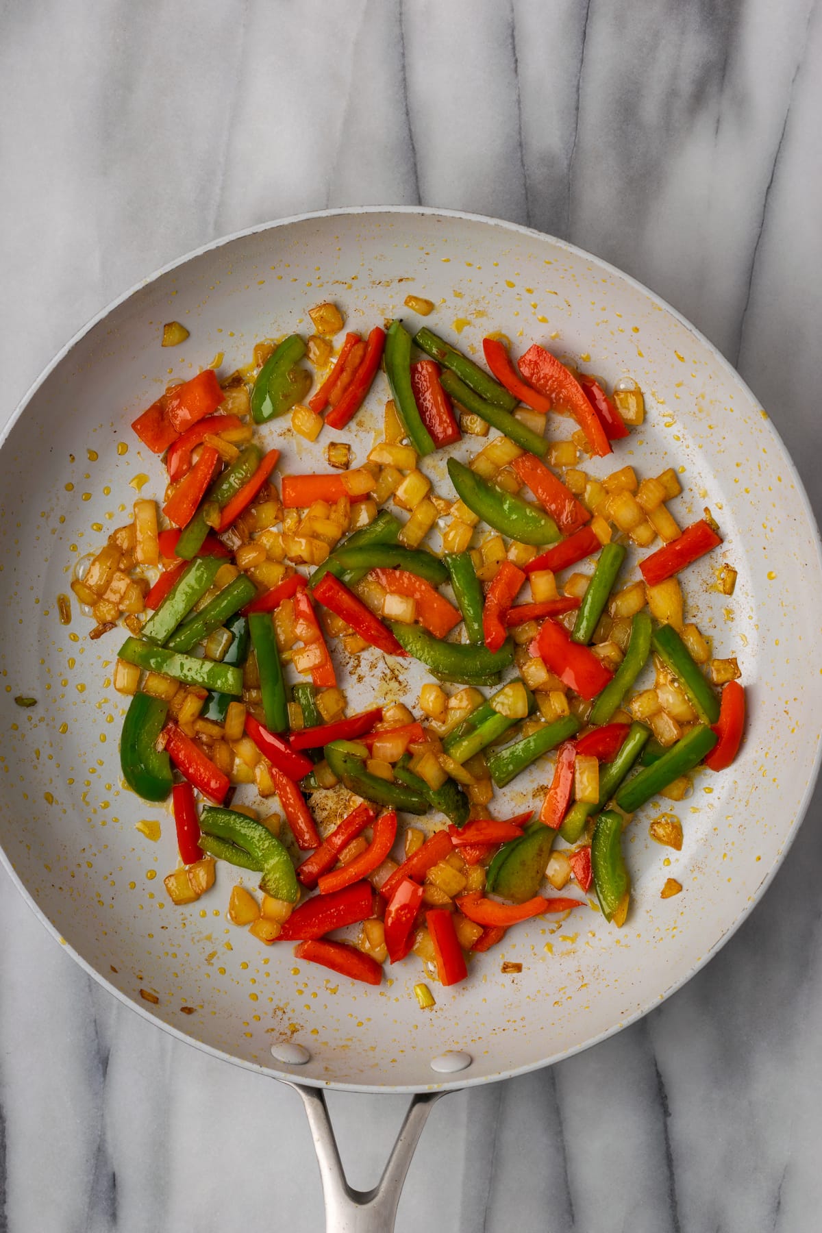 Overhead view of cooked red and green bell peppers, onions, and garlic in a skillet