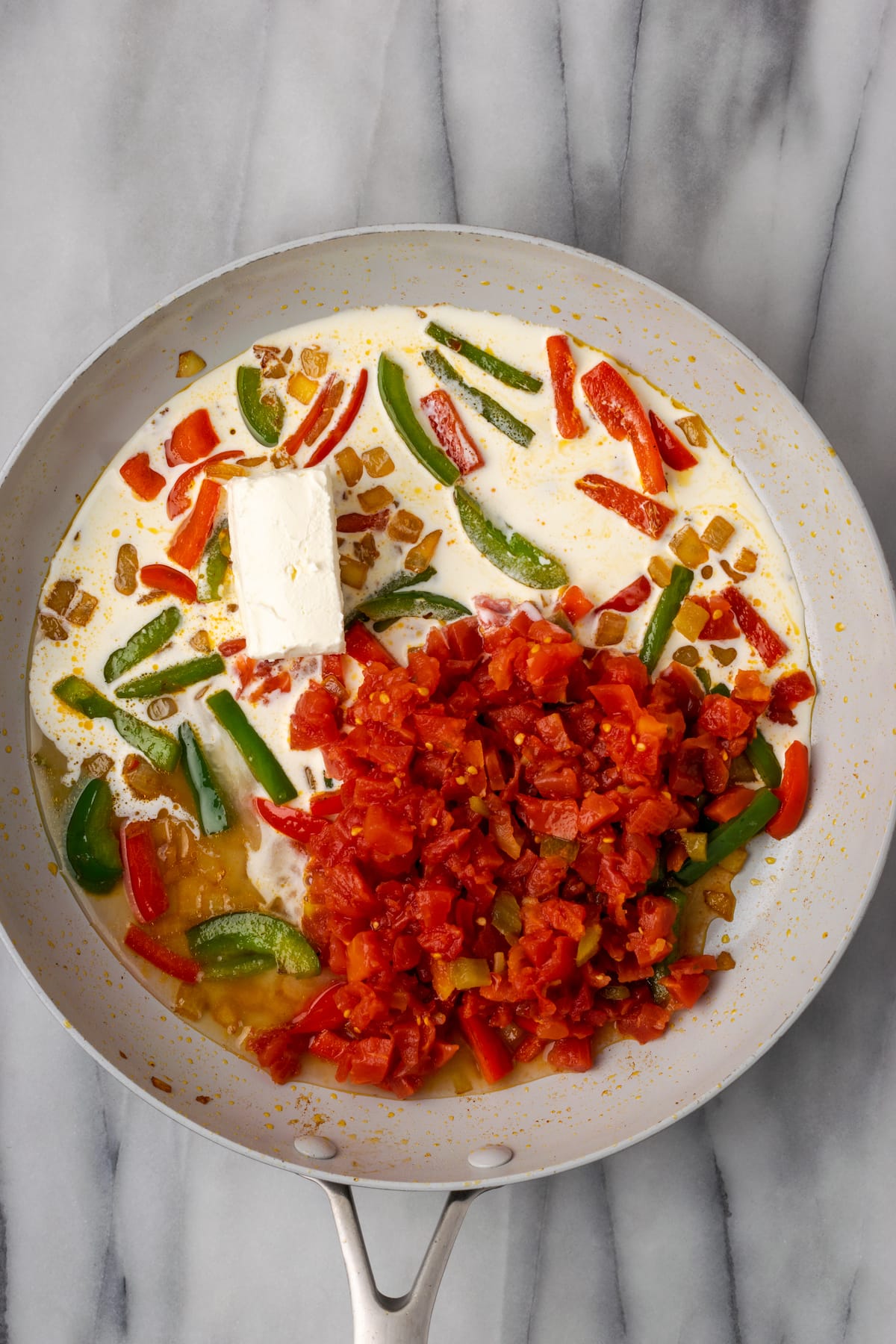 Overhead view of Ro-tel and cream cheese in a skillet on top of a cream sauce with bell peppers